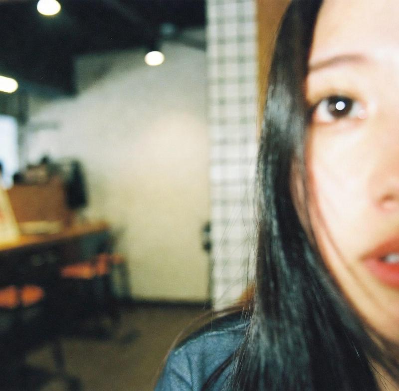 22歳の日本人女性が居酒屋にいる、雑な構図で顔がフレーム端で少し切れている、被写体がオフセンター、iPhoneで撮った粗い低画質写真、素人が撮った質の低い生写真