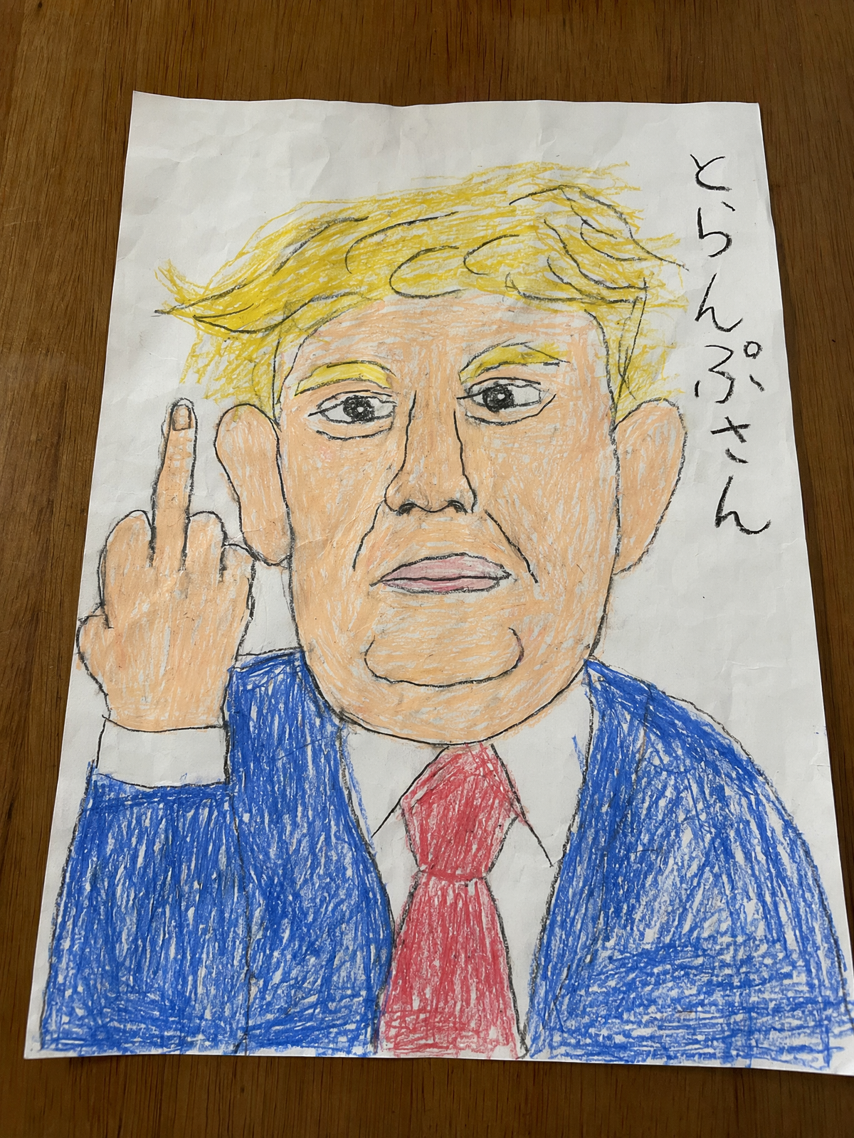 A realistic overhead photo of a childlike crayon drawing on a slightly wrinkled
