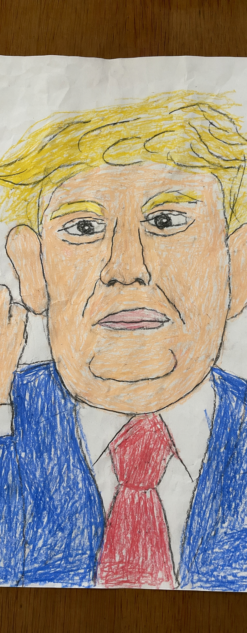 A realistic overhead photo of a childlike crayon drawing on a slightly wrinkled