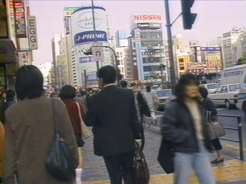 1990年の日本の渋谷を完全に再現した映像の1フレーム。 一人称視点で、渋谷の街を歩く人々を見ている。 画質や服装、広告、建物などは当時の日本の渋谷を完全に再現