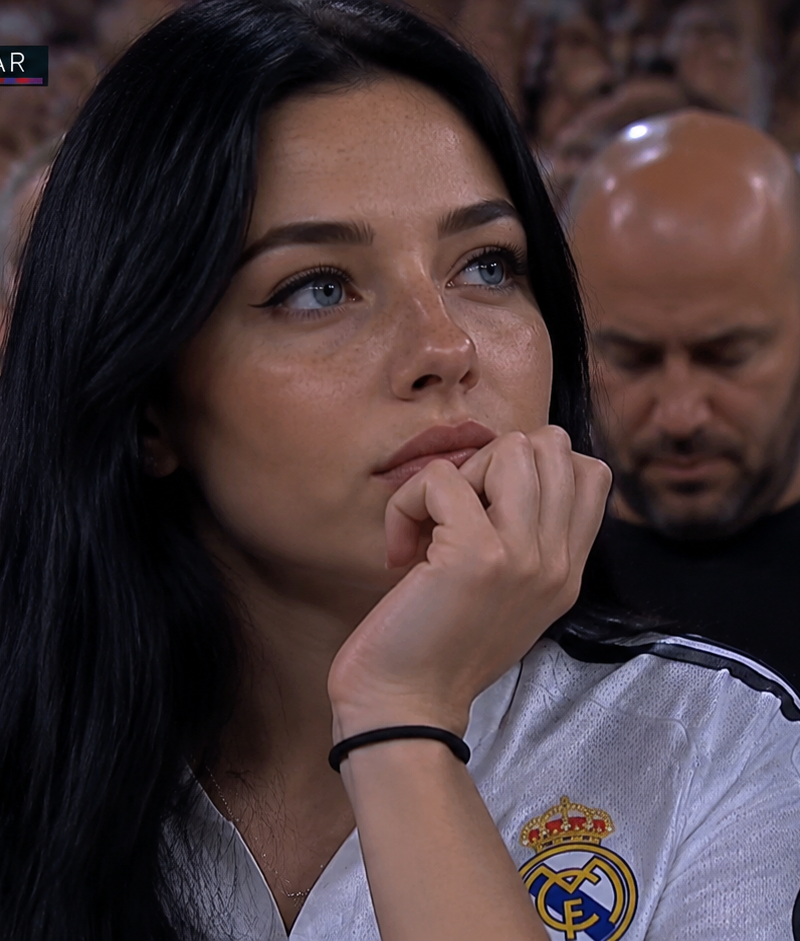 A high-definition, realistic broadcast shot of a young woman sitting in a crowde