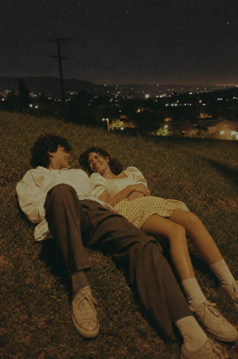 A cinematic vintage film photo of two young adults lying on a grassy hillside at