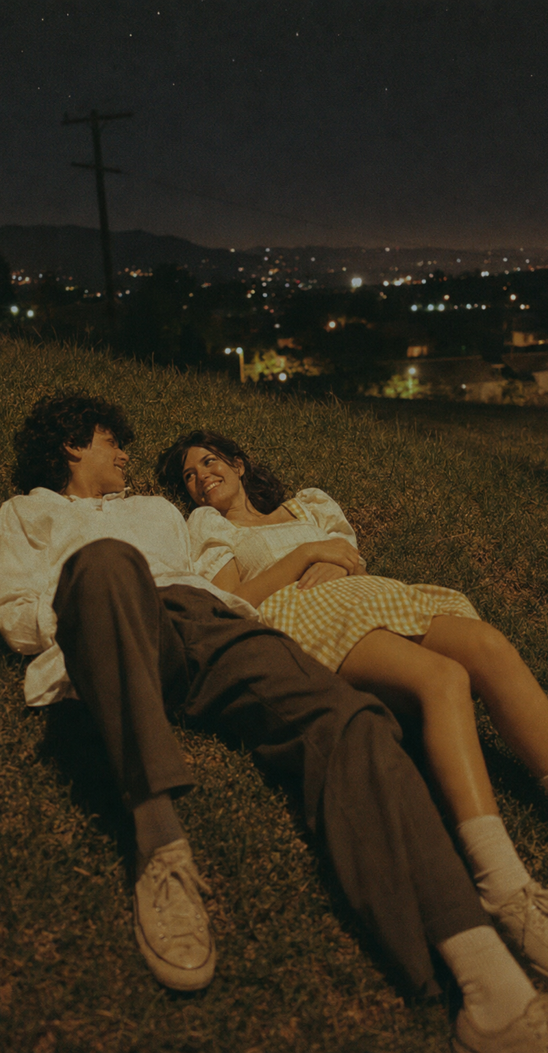 A cinematic vintage film photo of two young adults lying on a grassy hillside at