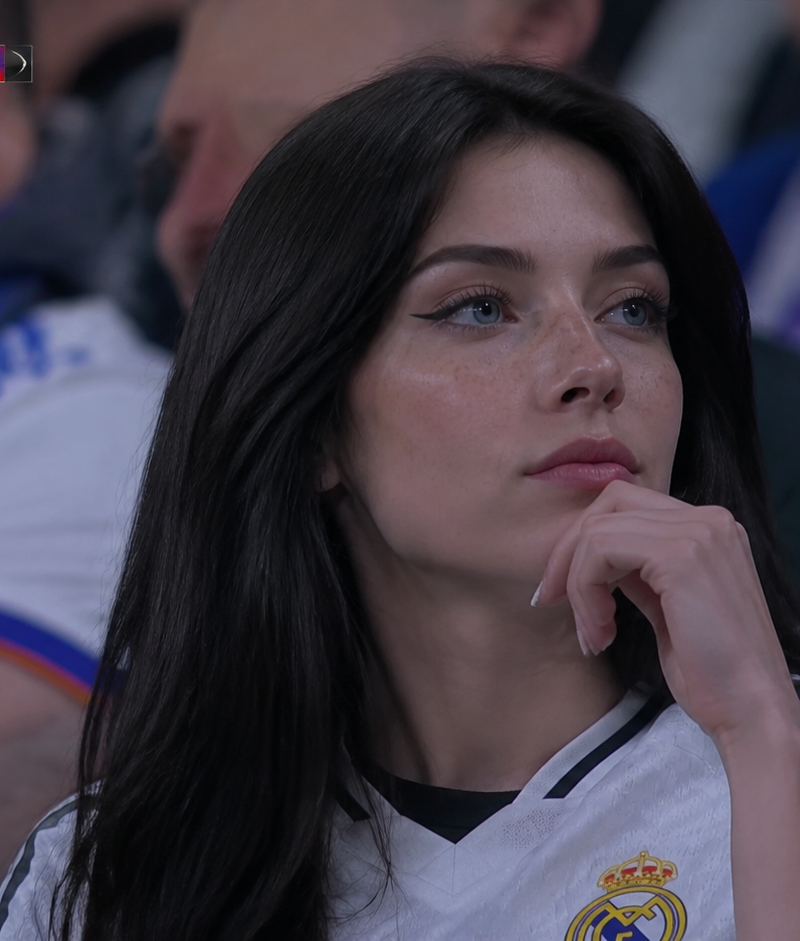 A high-definition, realistic broadcast shot of a young woman sitting in a crowde